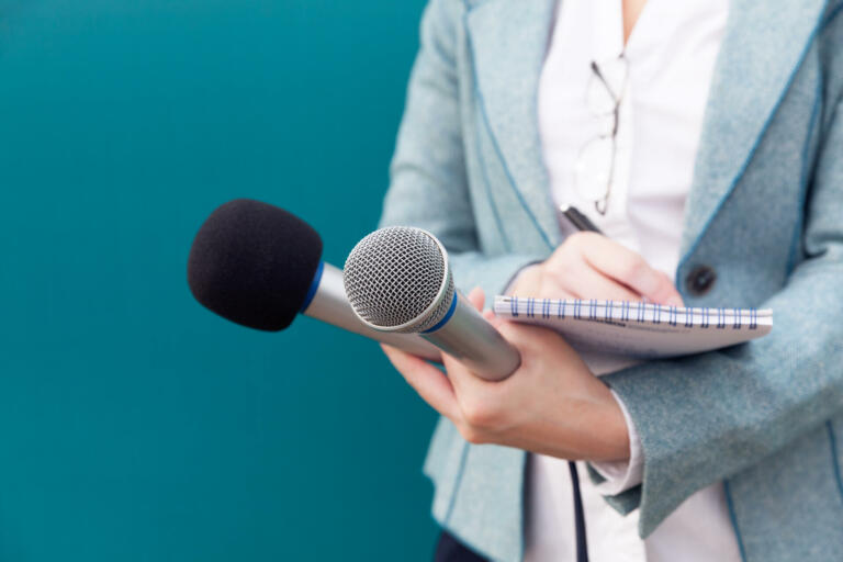 Reporter or TV journalist at news conference, holding microphone and writing notes