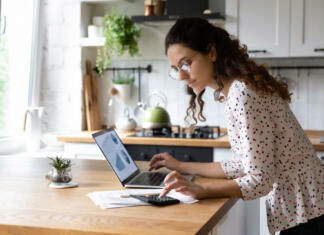 3 nasveti za optimalen začetek podjetniške poti Serious young woman wearing glasses calculating finances, household expenses, confident businesswoman working with project statistics, using laptop and calculator, standing in kitchen at home