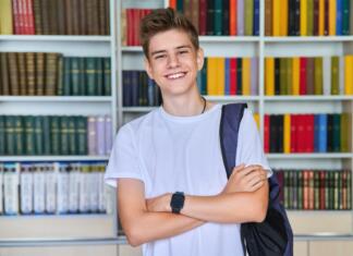Kaj nam prinaša status študenta? Single portrait of smiling confident male student teenager with backpack with crossed arms looking at camera in the library. School, education, knowledge, adolescence concept