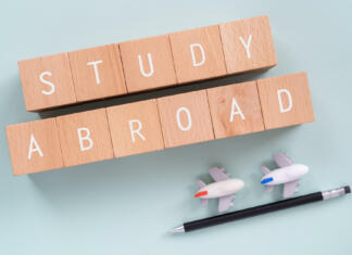 Podiplomski študij doma ali v tujini? Study Abroad; Wooden blocks with "STUDY ABROAD" text of concept, a pen, and plane toys.