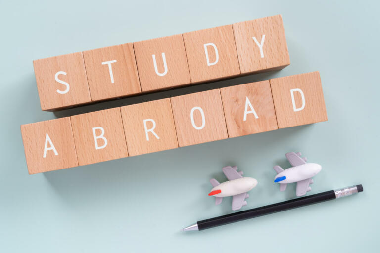 Study Abroad; Wooden blocks with "STUDY ABROAD"  text of concept, a pen, and plane toys.