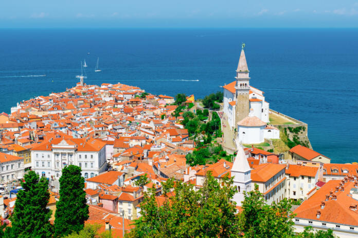 Travel to Slovenia. Cityscape of Piran with historic buildings and church. Adriatic sea in the background. Panoramic picture.
