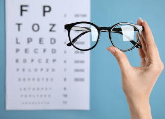 Je izbira očal na recept slaba? Woman holding glasses against eye chart on blue background, closeup. Ophthalmologist prescription