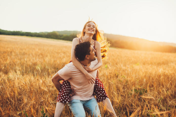 Young couple having fun in the wheat field. Piggy back rides. Family weekend.