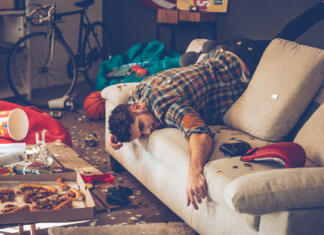 Kako čim hitreje pozdraviti mačka? Young handsome man passed out on sofa in messy room after party