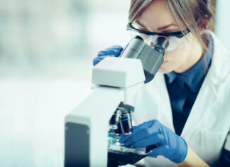 Za ženske v znanosti Young scientist looking through a microscope in a laboratory. Young scientist doing some research.