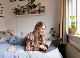 Kako do enoposteljne sobe v študentskem domu? Young university student following lecture on her laptop on the bed