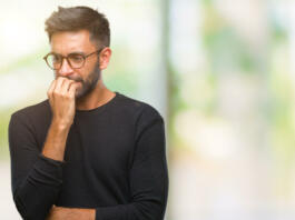 Adult hispanic man wearing glasses over isolated background looking stressed and nervous with hands on mouth biting nails. Anxiety problem.