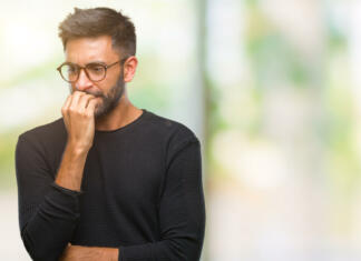 Družbeni problemi, ki pestijo moške Adult hispanic man wearing glasses over isolated background looking stressed and nervous with hands on mouth biting nails. Anxiety problem.