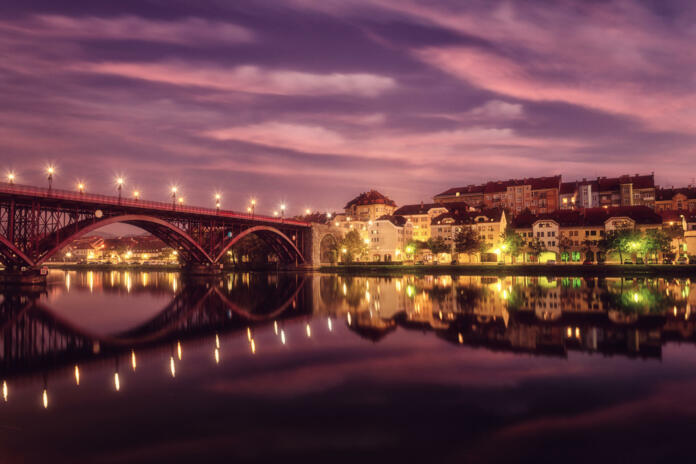 Amazing view of Maribor Old city, Main bridge (Stari most) on the banks of Drava river before sunrise, Slovenia. Scenic cityscape with dramatic cloudy sky and reflection, outdoor travel background