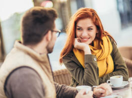 Attractive young couple in love sitting at the cafe table outdoors, drinking coffee