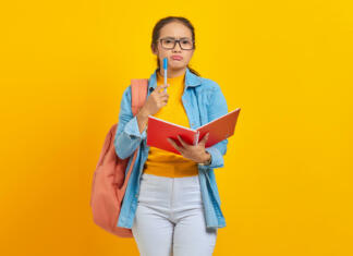 Bolonjski sistem, ki ga še vedno ne razumem! Beautiful young Asian woman student in casual clothes with backpack holding book and looks serious thinking about creative idea isolated on yellow background