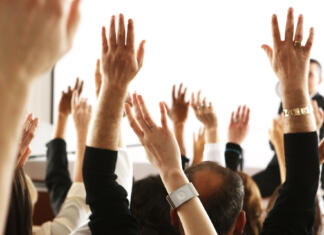 Veš, da so čez deset dni volitve? Big audience of people raising their hands to vote in favor of some topic.