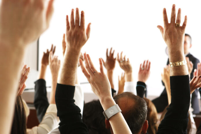 Big audience of people raising their hands to vote in favor of some topic.