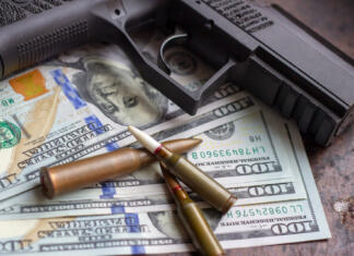 Nova zapora za financiranje terorizma v Sloveniji Black gun and weapon bullets on American dollars background. Military industry, war, global arms trade and crime concept