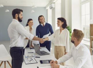 Inovativne oblike zaposlovanja mladih Business partners making deal, shaking hands in negotiation meeting. Smiling male CEO welcoming new female employee to company. Young boss congratulating happy woman with good results and promotion