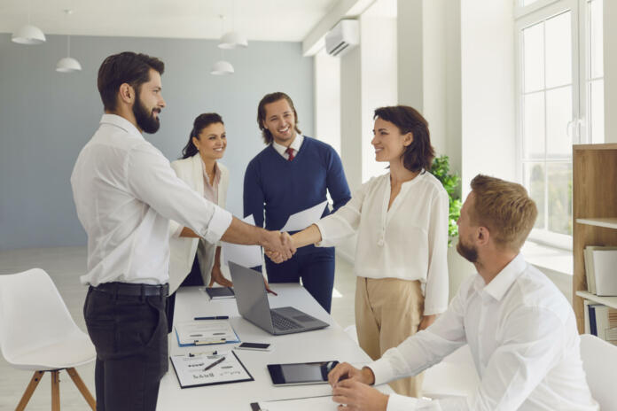 Business partners making deal, shaking hands in negotiation meeting. Smiling male CEO welcoming new female employee to company. Young boss congratulating happy woman with good results and promotion