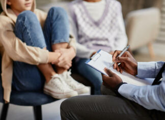 Kolikokrat (se) vprašate: »Kako se počutiš?« Close up of African-American psychologist taking notes on clipboard in therapy session for children
