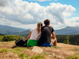 Couple of hikers admire view of Carpathian mountains. Happy tourists hug relaxing on top of Hoverla. Traveling in summer Ukraine