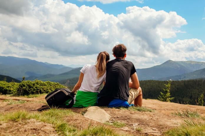 Couple of hikers admire view of Carpathian mountains. Happy tourists hug relaxing on top of Hoverla. Traveling in summer Ukraine
