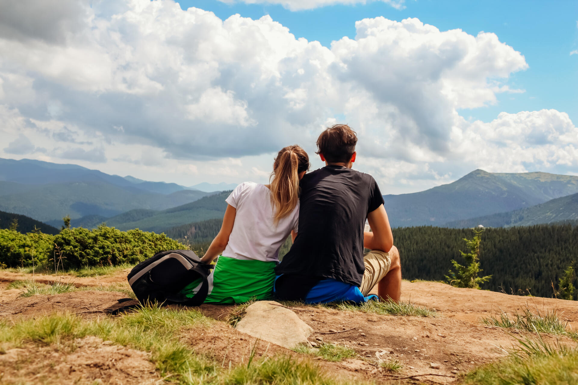 Couple of hikers admire view of Carpathian mountains. Happy tourists hug relaxing on top of Hoverla. Traveling in summer Ukraine