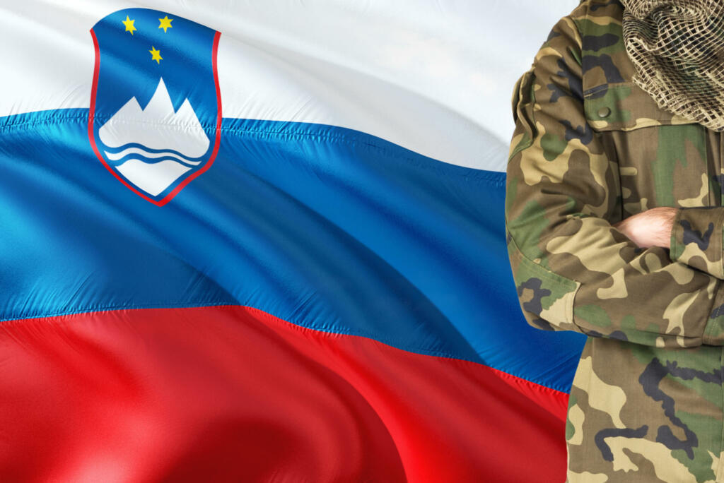 Crossed arms Slovenian soldier with national waving flag on background - Slovenia Military theme.