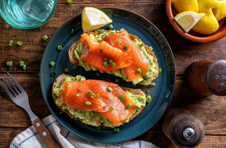 Delicious avocado and smoked salmon toasts on a rustic wood table top.