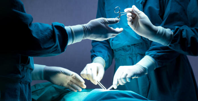 doctor and nurse medical team are performing surgical operation at emergency room in hospital. assistant hands out scissor and instruments to surgeons during operation.