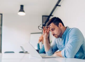 Kako se pripraviti na psihometrično testiranje? Exhausted young businessman using laptop at work and sitting by the desk while
