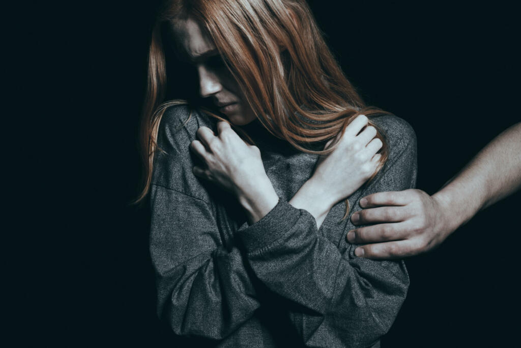 Fearful rape victim, man holding her arm, black background