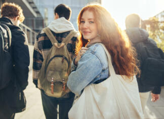 Kaj vse se spremeni, ko postaneš študent? Female student glancing back while going for a class in college. Girl walking with friends going for class in high school.