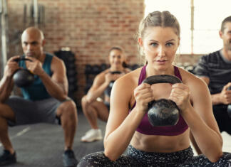 Vaje s kettlebelli: Najboljše vaje s kettlebelli Group of fit people holding kettle bell during squatting exercise at cross training gym. Fitness girl and men lifting kettlebell during strength training exercising. Group of young people doing squat with kettle bell.