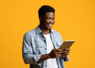 5 najboljših tabličnih računalnikov pod 200 € Happy african american millennial guy using modern digital tablet, looking at gadget screen and smiling on yellow studio background, black man gambling or shopping online, copy space