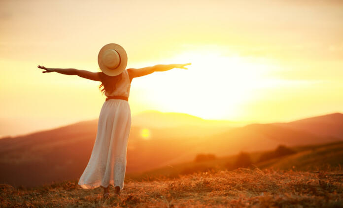 Happy woman standing with her back on the sunset in nature in summer with open hands