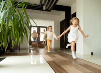 Ali si sploh želim imeti otroke? Happy young family with cardboard boxes in new home at moving day concept, excited children running into big modern own house hallway, parents with belongings at background, mortgage loan, relocation