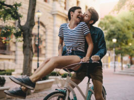 Laughing woman sitting on boyfriends bicycle handlebar. Cheerful couple on a bike together in the city having fun.