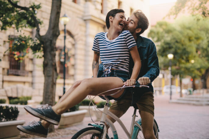 Laughing woman sitting on boyfriends bicycle handlebar. Cheerful couple on a bike together in the city having fun.