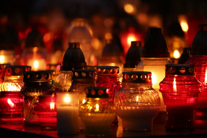 lot of bright, colorful candles standing on graves in the cemetery at night