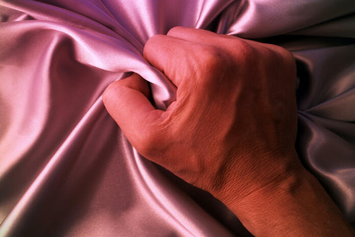 Man grabing satin sheet on the bed.