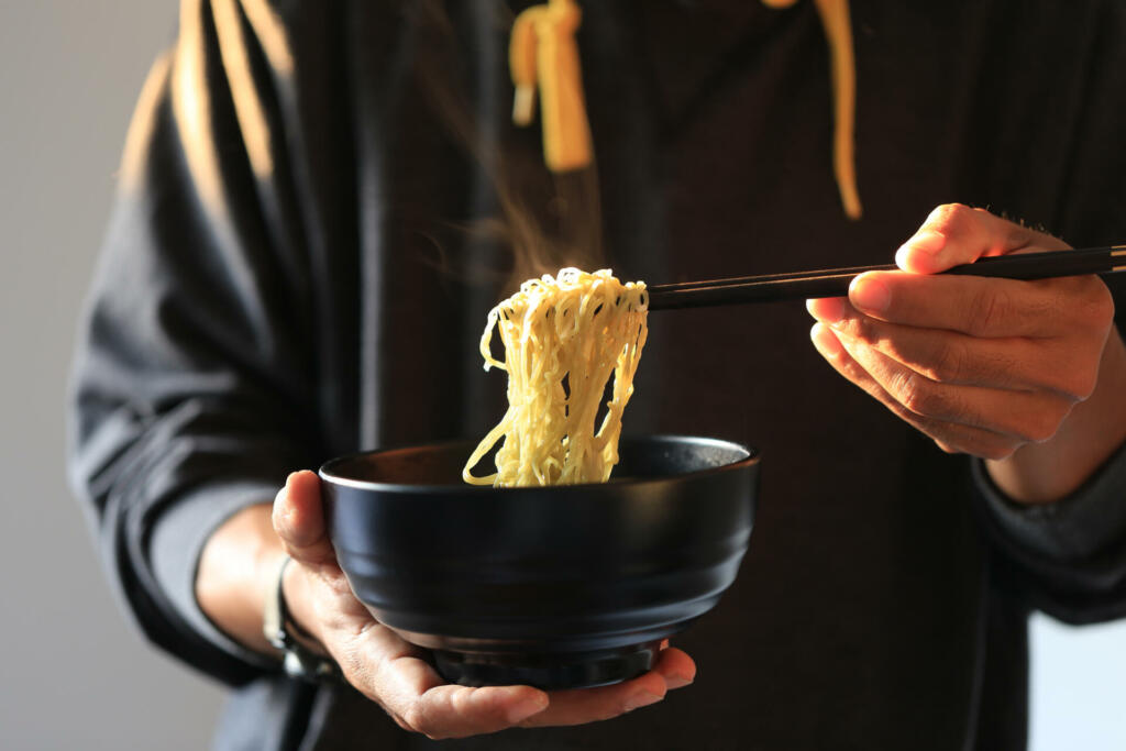 Man hand holding chopsticks of instant noodles in wood bowl with smoke rising in the home sunset background, Sodium diet high risk kidney failure, Healthy eating concept