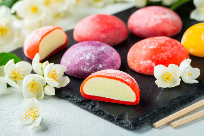 Multi-colored Japanese ice cream Mochi in rice dough and Jasmine flowers on a concrete blue background. Traditional Japanese dessert on a black slate.