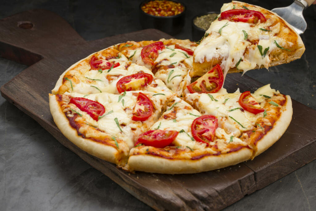 Pizza_Margerita, cheese pulling of home made delicious pizza made using tomato, basil leaf and mozzarella cheese as topping on thin pastry crust placed on a wooden board with grey background