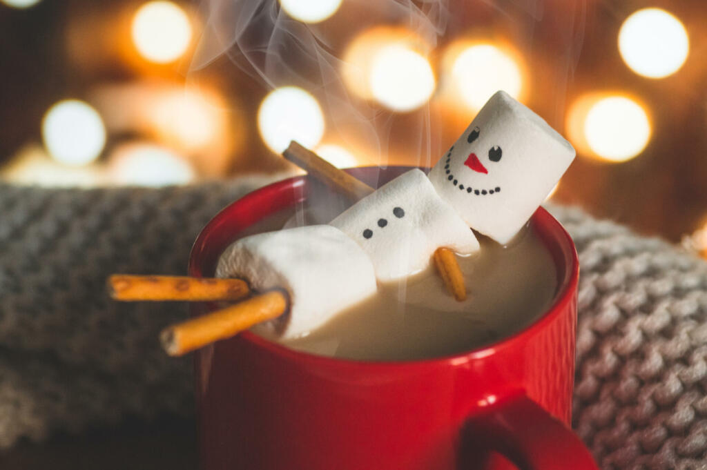 Red mug with hot chocolate with melted marshmallow snowman on bokeh background