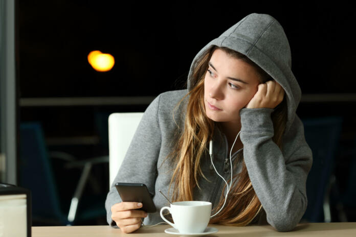 Sad pensive teenager listening to music in a bar in the night and looking at side