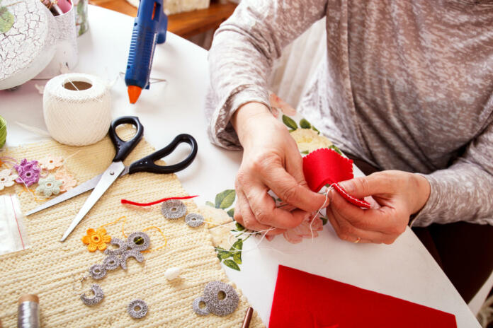 Senior women sews by hand and making heart shape ornament.