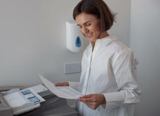 Ali kot študent potrebujem tiskalnik? Smiling woman worker scanning a document on photocopy machine In modern office. Blurred background