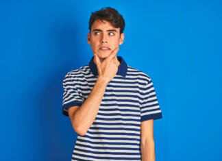 Ti neka beseda dela težave? Preveri, kaj pomeni! Teenager boy wearing casual t-shirt standing over blue isolated background Thinking worried about a question, concerned and nervous with hand on chin