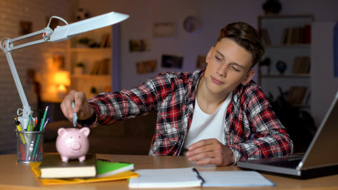 Teenager holding euro banknote putting it to piggyback, financial education