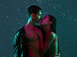 Tender kisses. Young couple, man and woman hugging, kissing under the rain over blue background in neon light. Concept of human emotions and feelings, love, passion, tenderness