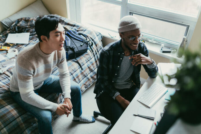 Two friends in a dorm room watching something on their computer screen.